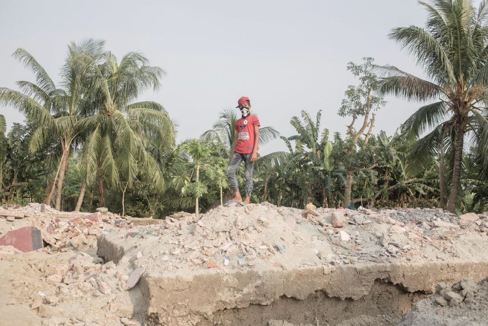 Boy standing on ruins, watching river erosion take place.