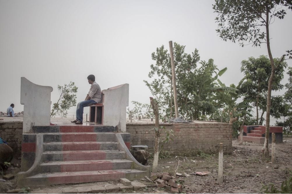 Sumon sitting on the remains of his dismantled house before it was lost to the river.